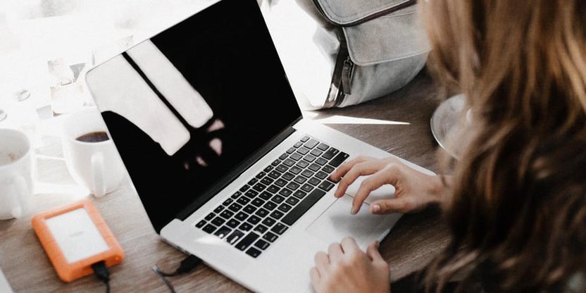 Bildet viser en dame som sitter og skriver på en laptop. Du ser damen fra, og hele tastaturet.