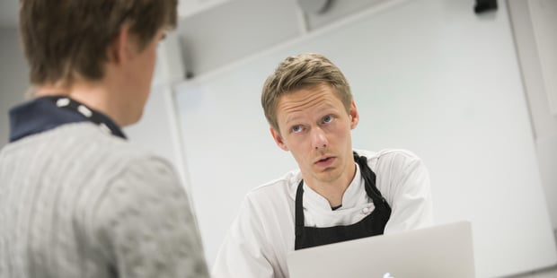 Mannlig lærer i samtale med elev, som sitter med ryggen til.