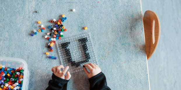Et barn som perler bokstaven U. Bildet er tatt ovenfra og vi ser bare litt av hodet og to hender.