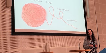 Foto av Marte Balas foran en skjerm med power point. Motivet på skjermen er en rød tråd