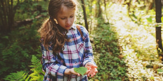 Jente som holder et blad i hånden ute i en skog.