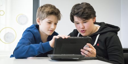 To gutter sitter med en Ipad ved en pult.