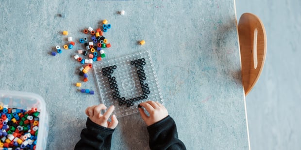 Et barn som perler bokstaven U. Bildet er tatt ovenfra og vi ser bare litt av hodet og to hender.