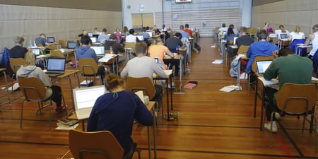 Mange elever sitter på pulter med ryggen til i et eksamenslokale.