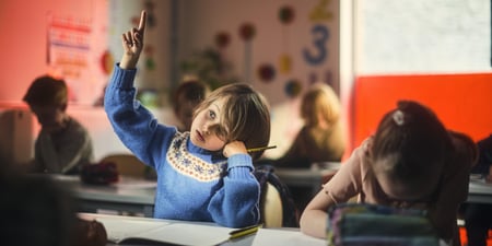 Barn som sitter i et klasserom og rekker opp hånda for å få oppmerksomhet