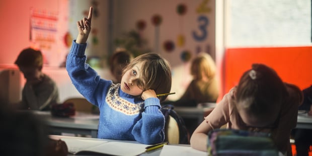 Barn som sitter i et klasserom og rekker opp hånda for å få oppmerksomhet