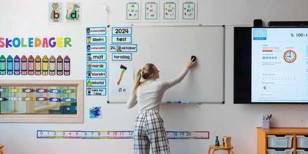 En kvinnelig lærer som står og fjerner noe fra smartboardet. Vi ser henne bakfra.