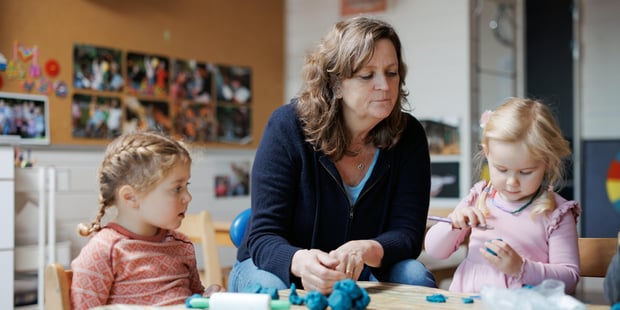Barnehagelærer sitter med to barn ved bordet og leker med naturgummi. Inne