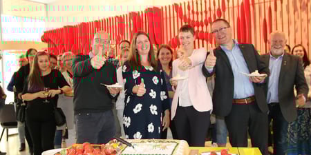 En gjeng med mennesker smiler mot kamera og feirer med å spise kake.