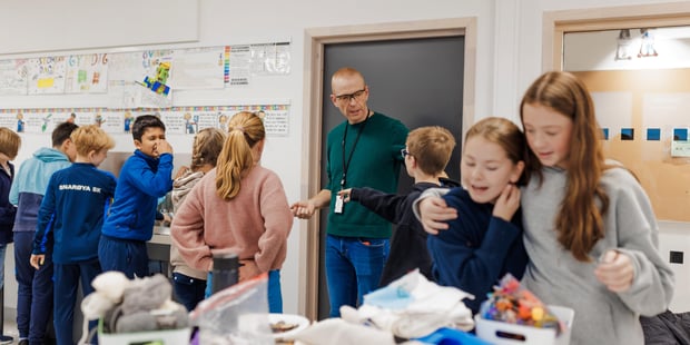 Bildet viser elever ved Oksenøya barneskole, 1. og 6. klasse i 2024. Mange elever vasker hendene, mens læreren gir instruksjoner inne i håndarbeidssalen.