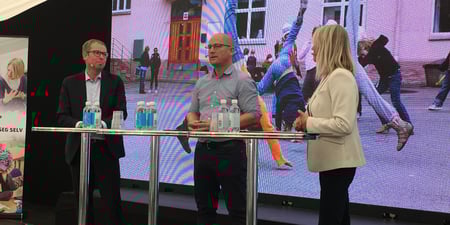 To menn og en dame står ved et høyt bord og snakker.