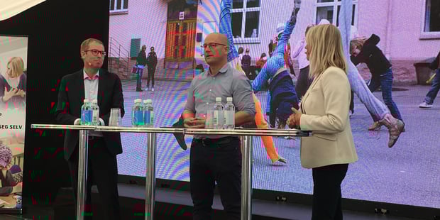 To menn og en dame står ved et høyt bord og snakker.