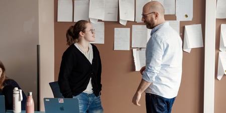 To personer i prat står foran en oppslagstavle. Illustrasjonsfoto