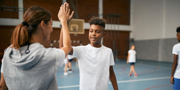 En elev gir high five til sin kroppsøvingslærer i en gymsal. Læreren står med ryggen til.