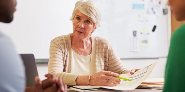 Senior teacher at desk talking to adult education students