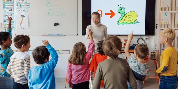 Bildet viser elever ved Oksenøya barneskole, 1. og 6. klasse i 2024. En stor gruppe står foran læreren sin og rekker hånda i været. Vi ser elevene bakfra, læreren forfra.