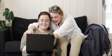 To kvinner som smiler i sofa med pc