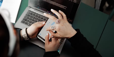 Nærbilde av tre hender og en pc og en mobiltelefon. Til venstre for pc-en ligger det et hefte. Illustrasjonsfoto