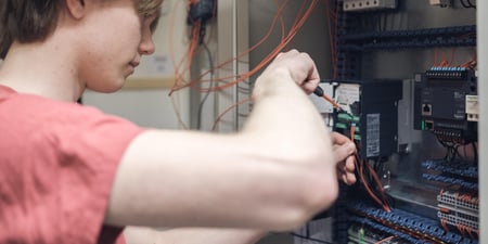 En elev på yrkesfag skrur med en skrutrekker inni et elektrisk skap med sikringer og ledninger. Illustrasjonsfoto