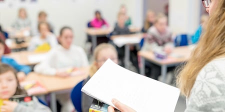 Biletet syner eit klasserom med elevar, og ein kan skimte ein lærar heilt fremst.