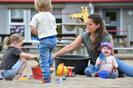Foto av kvinnelig barnehagelærere som sitter og leker med tre barn