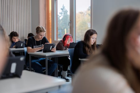 Foto av elever på ungdomsskole. De sitter i klasserommet og jobber konsentrert på ipad. Illustrasjonsfoto