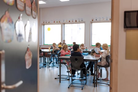 Bildet viser elever ved Oksenøya barneskole, 1. og 6. klasse i 2024. Disse små barna sitter i klasserommet og spiser nistepakken sin.