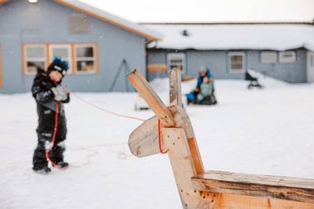 Barn ute i barnehagen på vinteren som kaster lasso mot et reinsdyr laget av tre