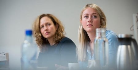 To personer som sitter rundt et bord og lytter. Foto. 