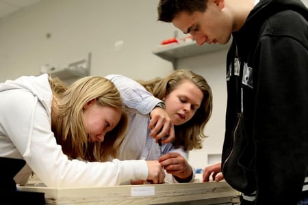 To personer skrur på noe, mens en tredje person ser på. Foto. 