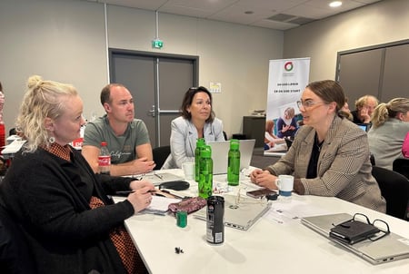 Personer sitter rundt et bord og samtaler