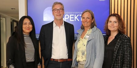Tre kvinner og én mann ser mot kameraet foran en vegg der det står Spekter.