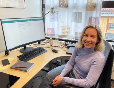 Bilde av Kristine smilende foran skjermen på kontoret.
