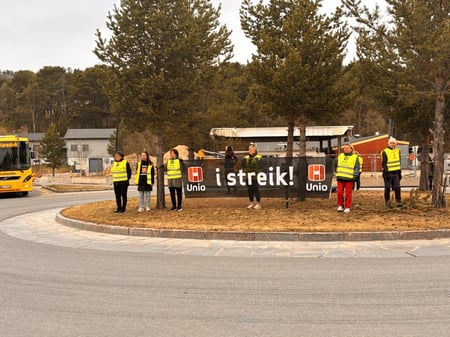 streikende Uniomedlemmer markerer ved å stå i rundkjøring i Karasjok med banner der det står Unio i streik. Noen har gule Uniovester med påtrykk streikevakt og noen viser sort skjorte med Uniotrykk.