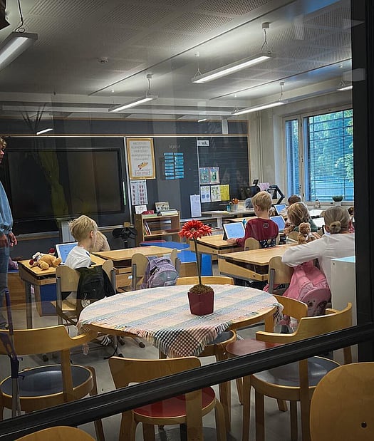 Bilde tatt utenfra og inn gjennom et vindu til et finsk klasserom. Vi ser bakhodet på elever som jobber med en oppgave. 