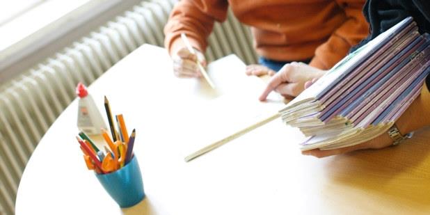 Deler av en elev som sitter ved et bord og gjør skoleoppgaver.