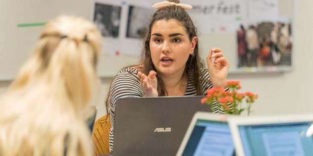 Studenter sitter rundt et bord med datamaskin og diskuterer