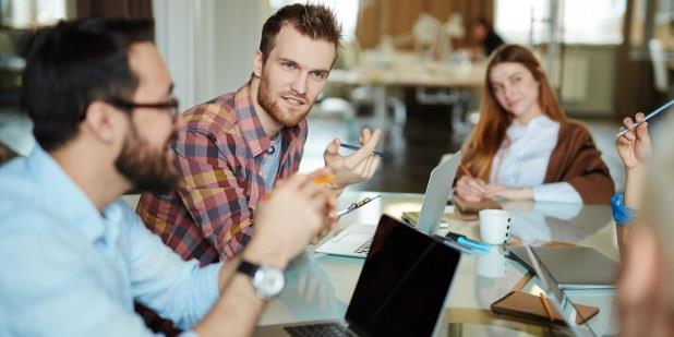 Tre personer diskuterer rundt et bord. Foto.