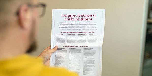 Mann leser plakat med tittel: "Lærerprofesjonens etiske plattform". Foto.  