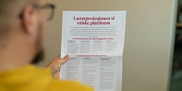 Mann leser i plakaten med overskriften "Lærarprofesjonen si etiske plattform". Illustrasjon.