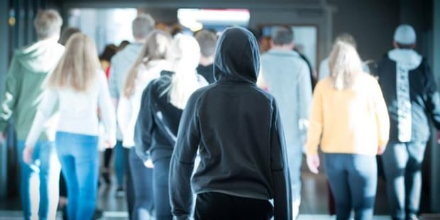Bilde av en elev bakfra med hette på hodet som står i utgangen av en stor gruppe elever som er på vei inn en dør. Illustrasjonsfoto