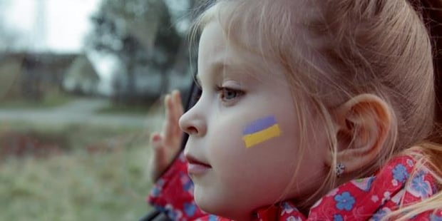foto av en jente som titter ut av et togvindu, hun har et ukrainsk flagg malt på kinnet sitt.