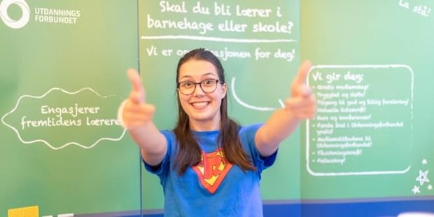 Bilde av en pedagogstudent med PS-t-skjorte. Hun har armene utstrakt og ser rett i kamera.