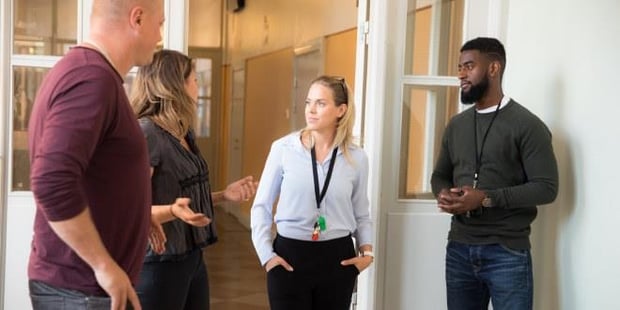 Bilde av en gruppe lærere som står og snakker sammen i en korridor på en skole. Illustrasjonsfoto
