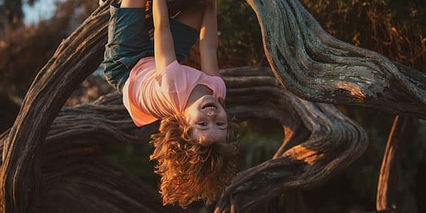 En smilende jente som henger med hodet ned fra en gren. Illustrasjonsfoto
