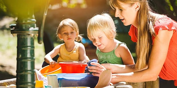 En interessert barnehagelærer leker sammen med barna ute i sola. Mostphotos.