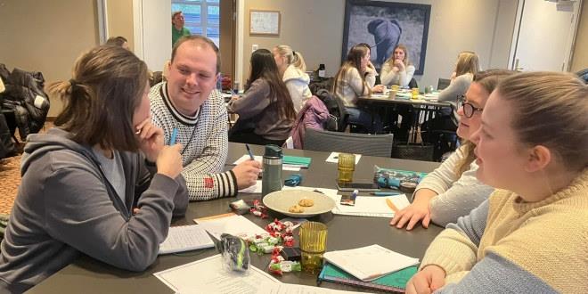 Vi ser personer som sitter rundt et bord og diskuterer.