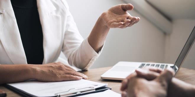 Bilde av en person som sitter ved et bord og gestikulerer.