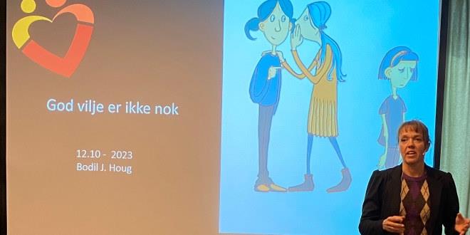 Bilde av Bodil J. Houg i halvfigur som står foran et lerret med teksten God vilje er ikke nok