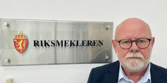Terje Skyvulstad avbildet foran skiltet til Riksmekleren. Han ser alvorlig ut. 